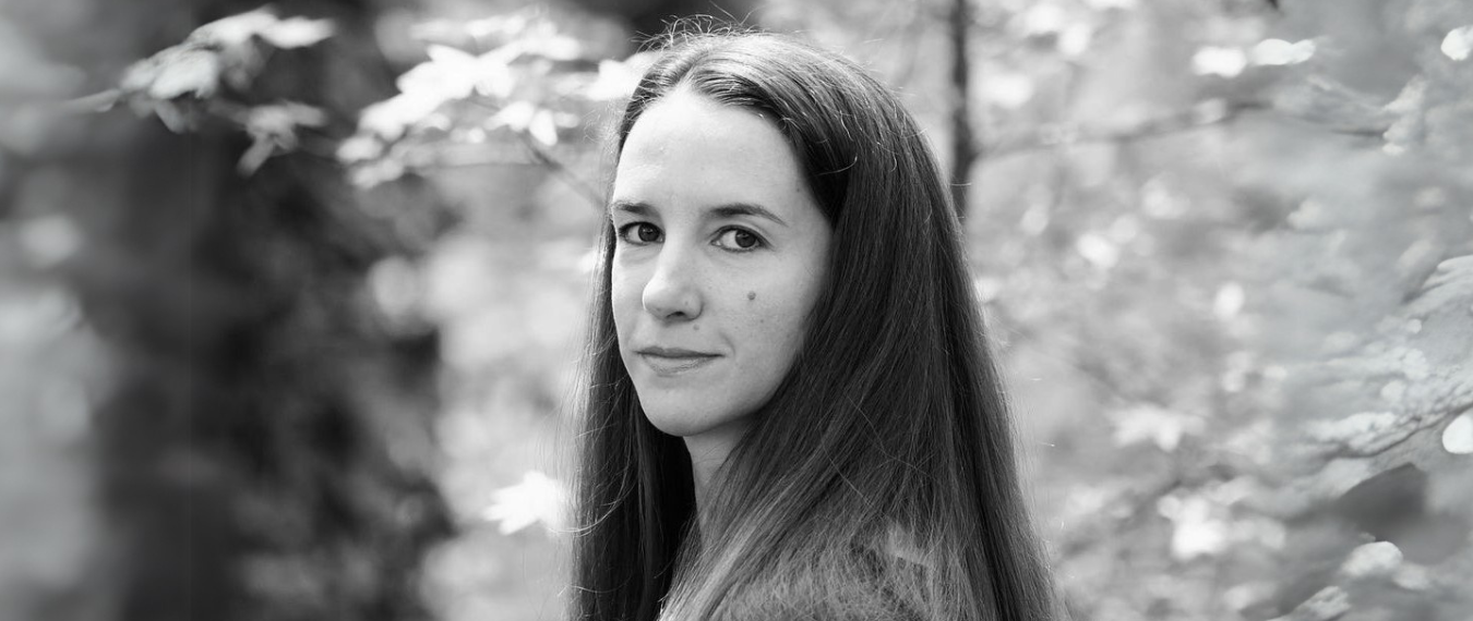 A grayscale photograph of a woman with dark hair standing in front of a nature scene