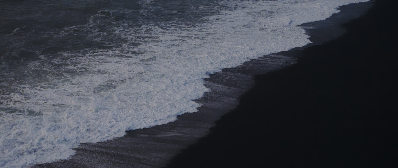 A grayscale photo of an ocean wave hitting sand