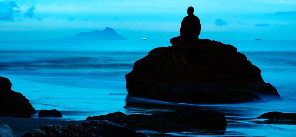 person sitting on a rock looking over the ocean