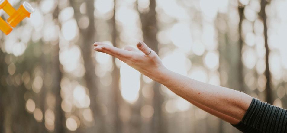 woman's outstretched arm with trees in background and bottles of pills off to the side