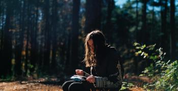 woman writing in journal over the woods