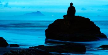 person sitting on a rock looking over the ocean