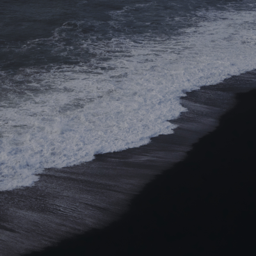 A grayscale photo of an ocean wave hitting sand