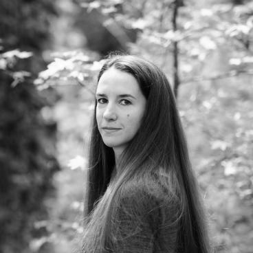 A grayscale photograph of a woman with dark hair standing in front of a nature scene